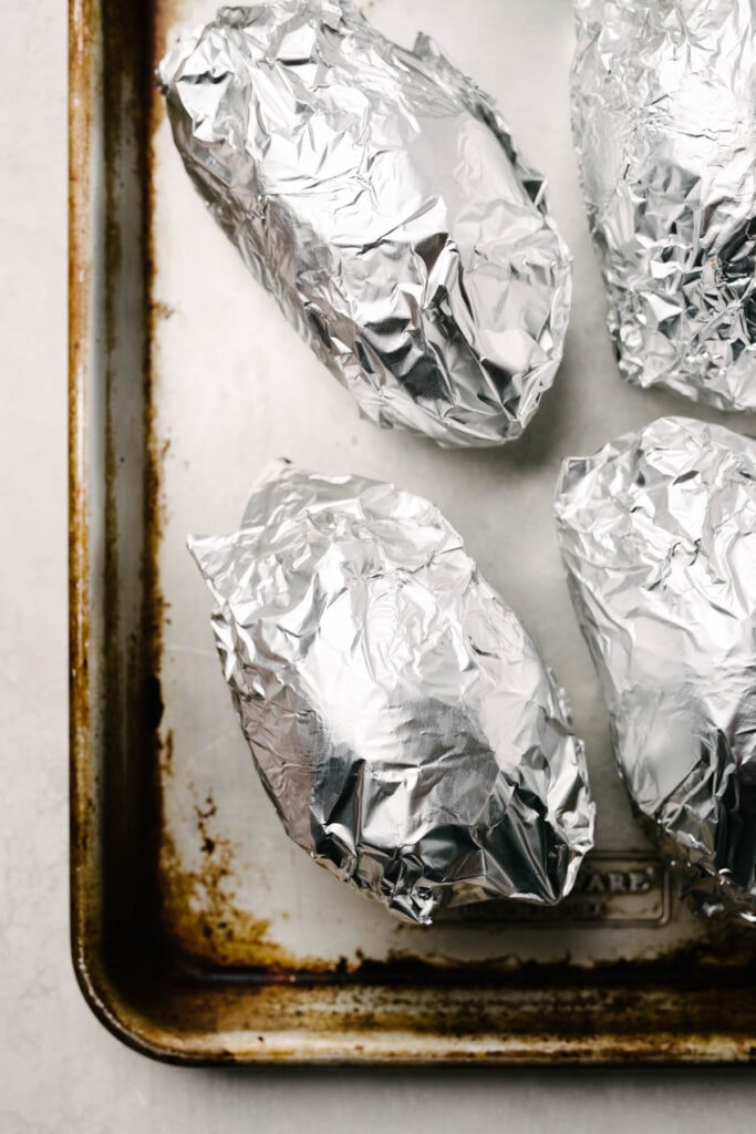 Sweet potatoes wrapped in foil on a baking sheet. 