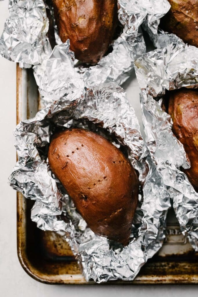 A baking sheet with baked sweet potatoes in open tinfoil. 