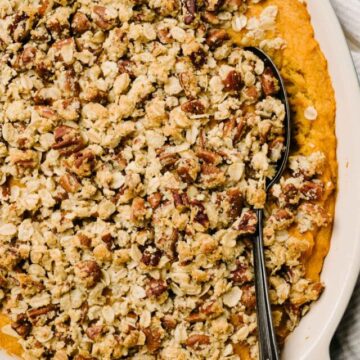 Baked sweet potato casserole with mashed sweet potatoes and pecan streusel on top, with a spoon in it.