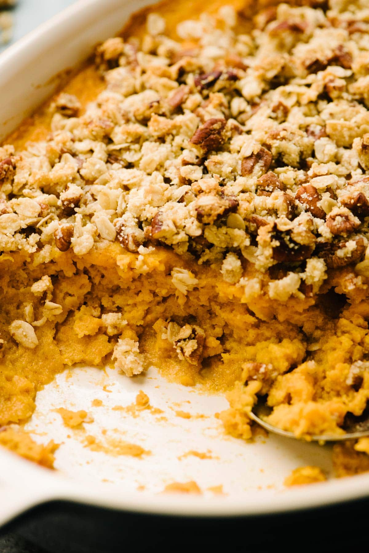 Side view, healthy sweet potato casserole topped with pecan streusel in a casserole dish.