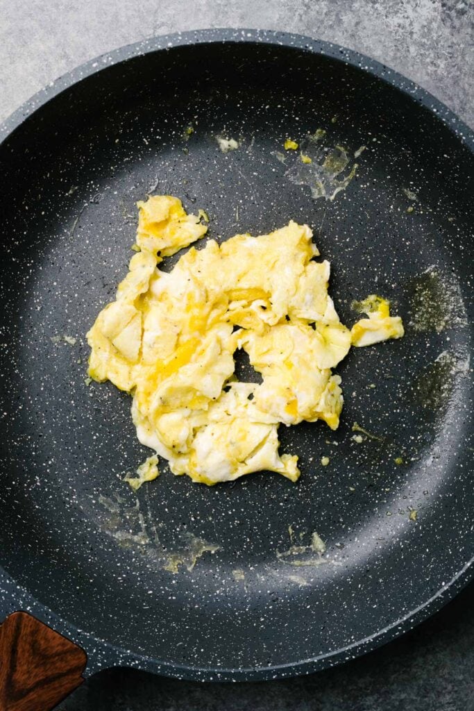Scrambled eggs in a dark grey skillet.