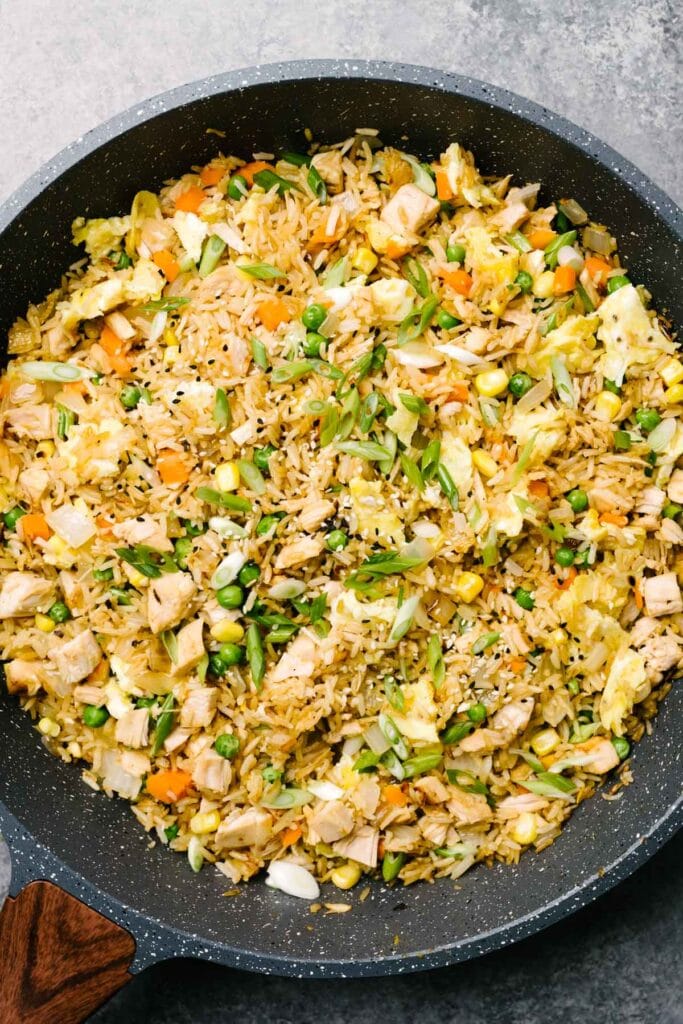 Turkey fried rice garnished with green onions and sesame seeds in a dark grey skillet.