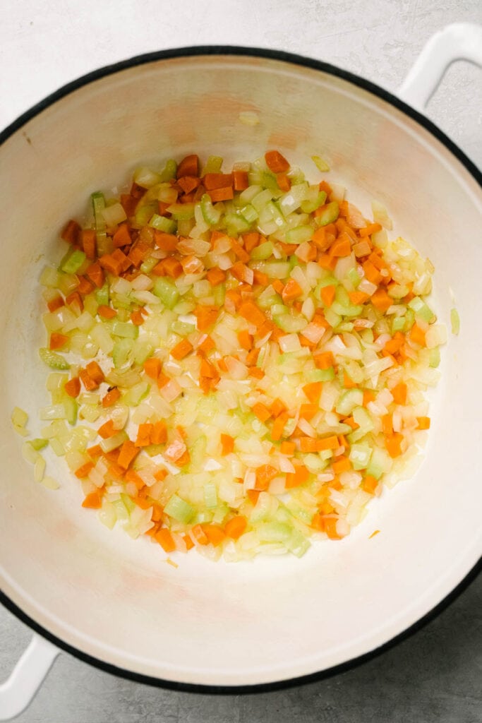 Diced onion, carrot, and celery sautéed in coconut oil in a white dutch oven.