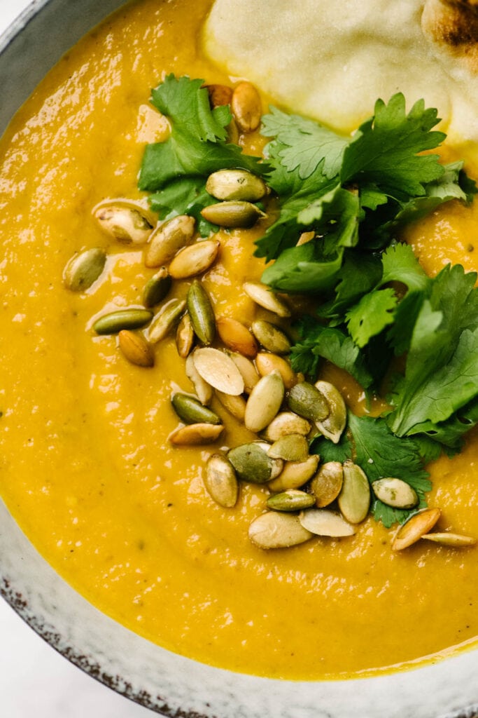 A bowl of pumpkin curry soup garnished with pumpkin seeds and cilantro.
