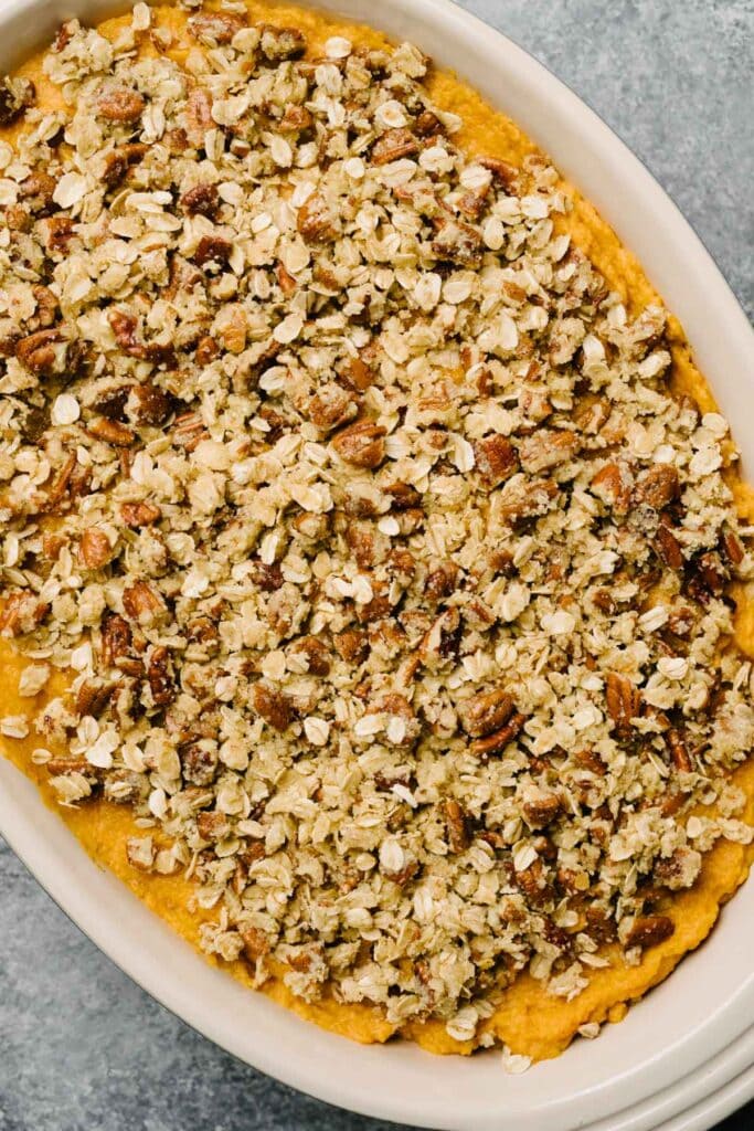A baking dish with mashed sweet potatoes and a layer of pecan topping on top, ready to bake. 