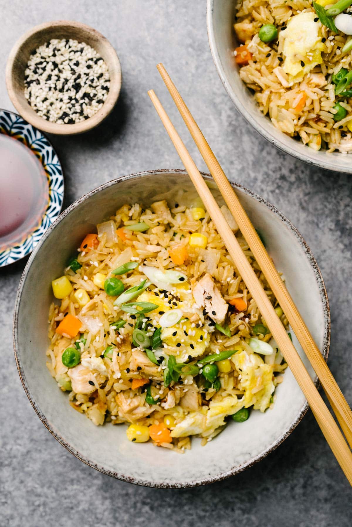 Two bowls of leftover turkey fried rice on a marble background, with small bowls of soy sauce and sesame seeds to the side.