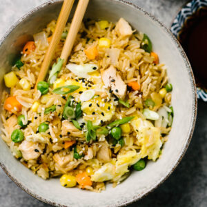 A pair of chopsticks tucked into a bowl of turkey fried rice.
