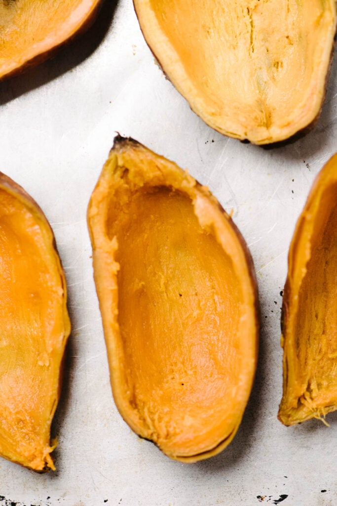 Sweet potato halves on a baking sheet with most of the insides scooped out. 