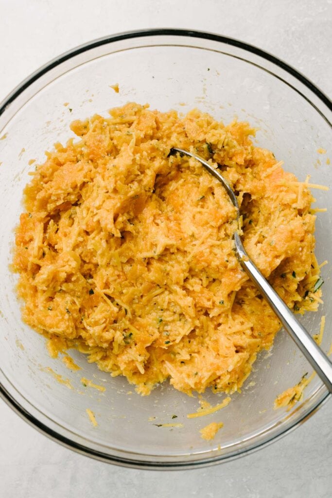 A spoon mixing ingredients into a bowl of mashed sweet potato flesh. 