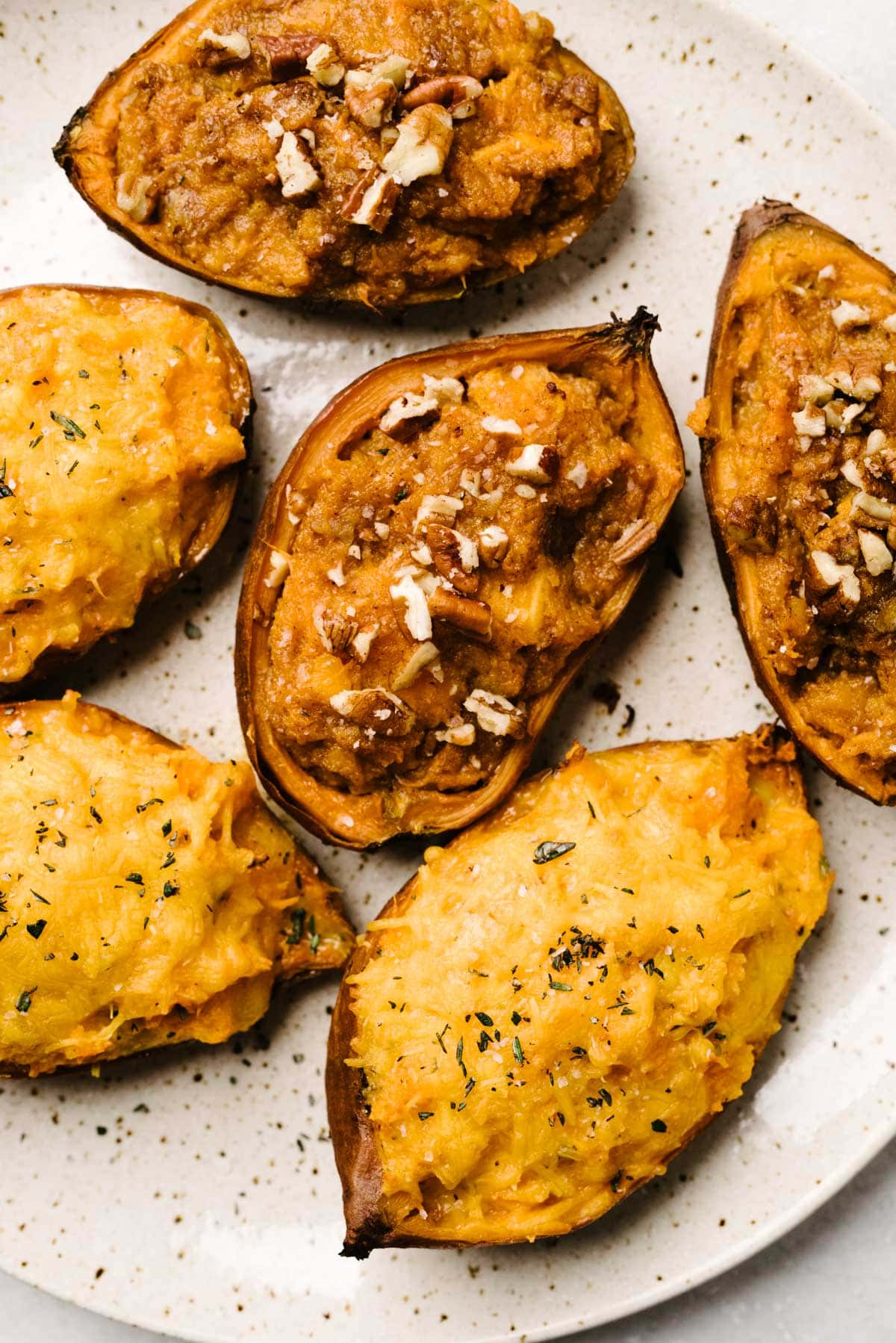 Two variations of twice baked sweet potatoes, one savory and one sweet, on a cream speckled plate.