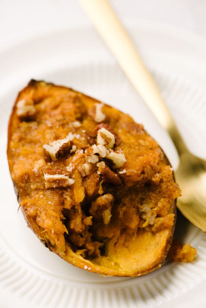 Side view, twice baked sweet potatoes with maple syrup and pecans on a small white plate with a gold spoon.