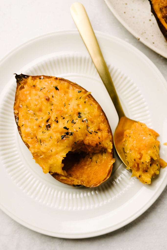 Side view, savory twice baked sweet potatoes with cheddar cheese and rosemary on a small plate with a gold spoon.