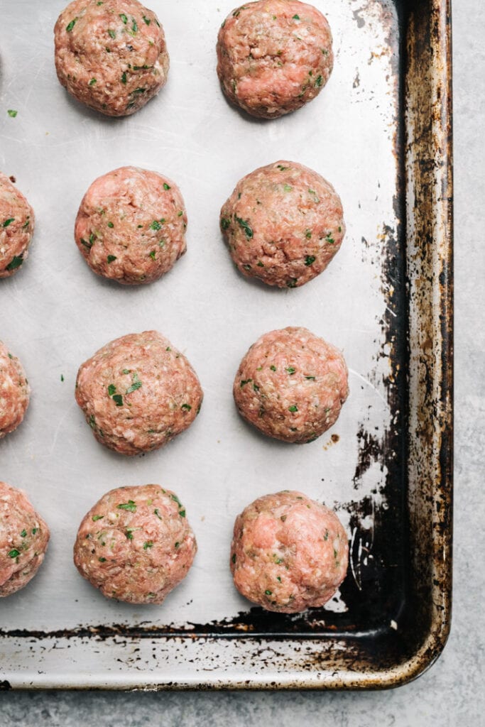 Raw Italian style meatballs formed on a baking sheet before cooking.