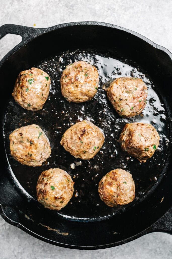Healthy meatballs being pan seared in a cast iron skillet to brown the outsides and help form a flavorful crust.