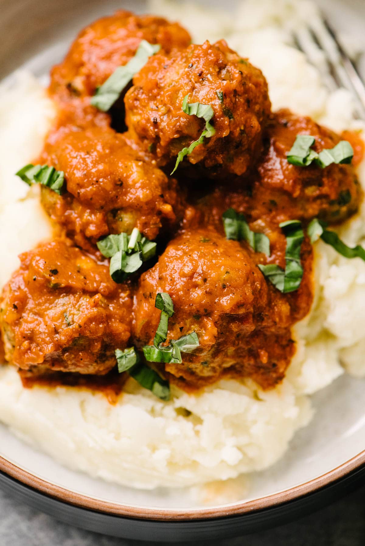 Side view, healthy turkey meatballs over mashed potatoes in a low bowl, garnished with fresh basil.