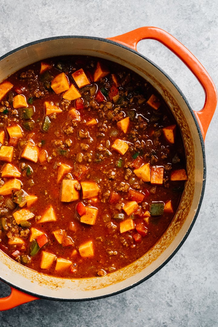 Healthy chili with ground beef and sweet potatoes in a dutch over before simmering.
