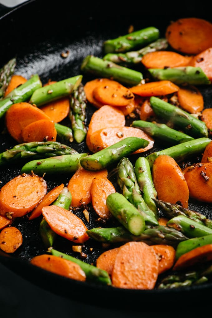Side view, stir fried asparagus and carrots in a cast iron skillet.