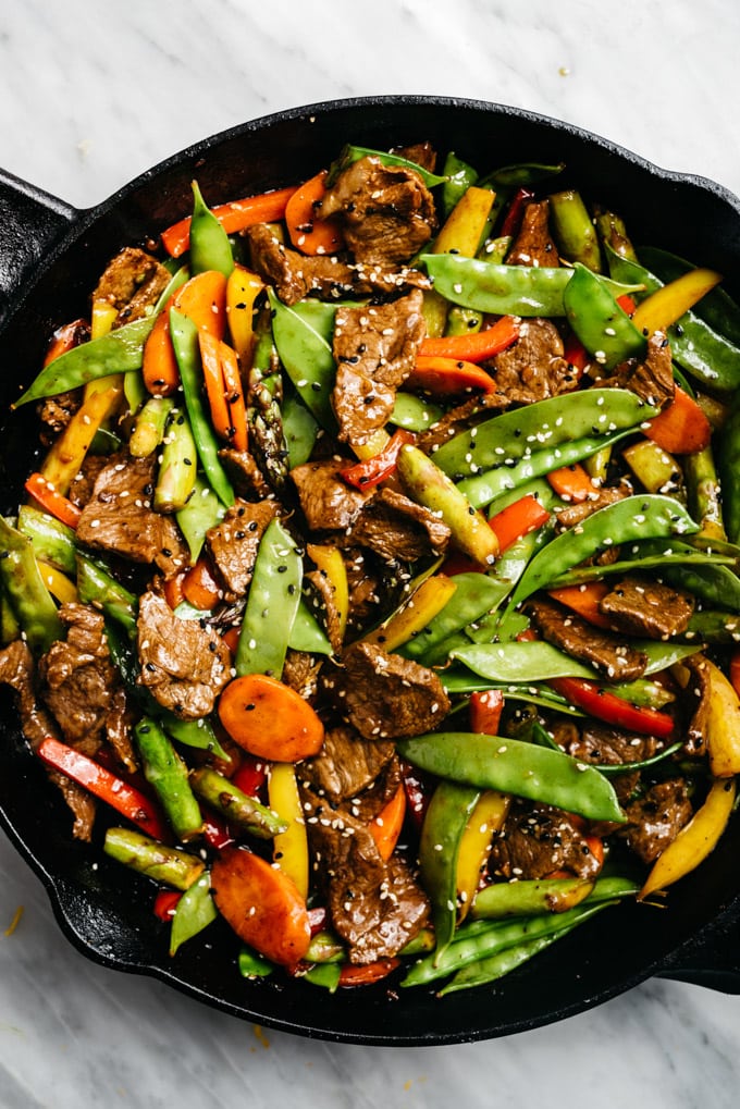 Beef stir fry with vegetables and healthy homemade stir fry sauce in a cast iron skillet on a marble table.