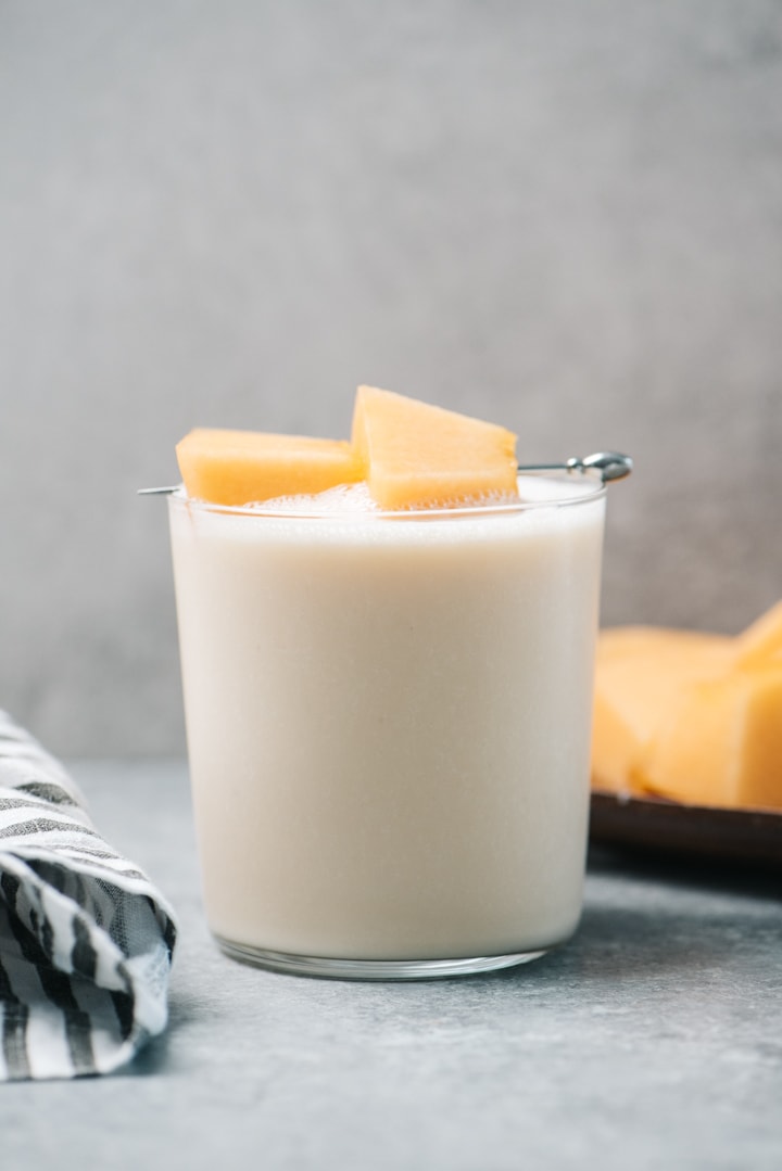 Side view, a cantaloupe smoothie in a glass garnished with fresh cantaloupe chunks.