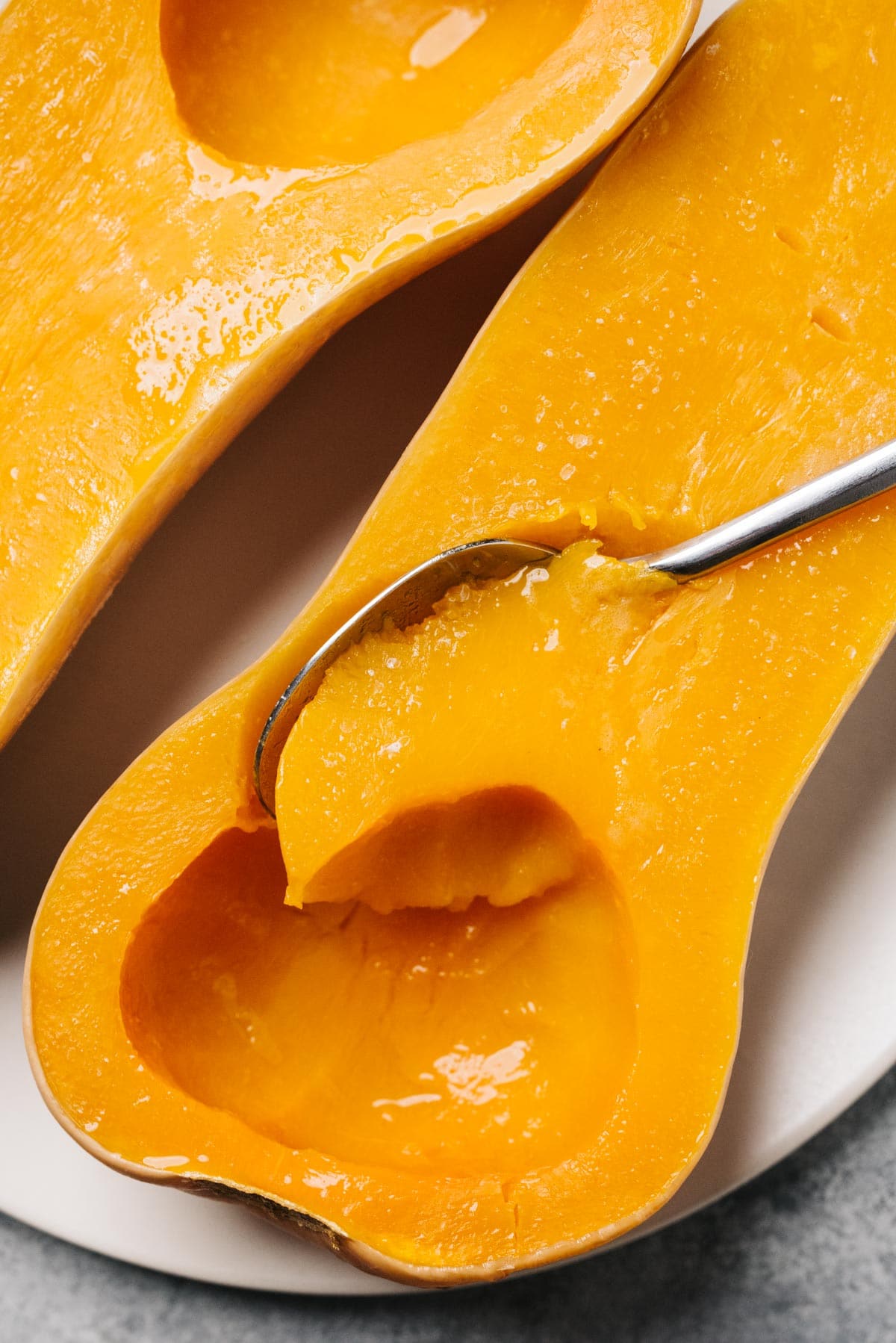 A spoon tucked into a butternut squash halve cooked in a crockpot, showing the creamy, buttery texture.