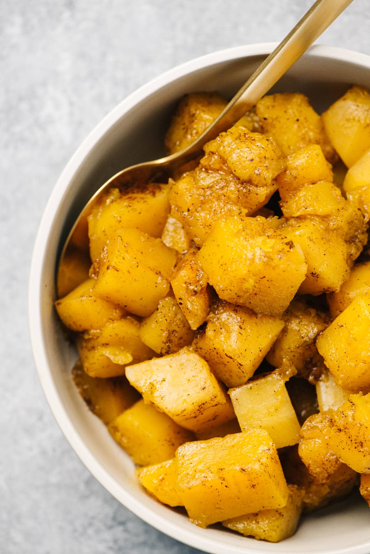 Diced pieces of slow cooker butternut squash seasoned with brown sugar and warming spices in a tan serving bowl with a gold spoon.