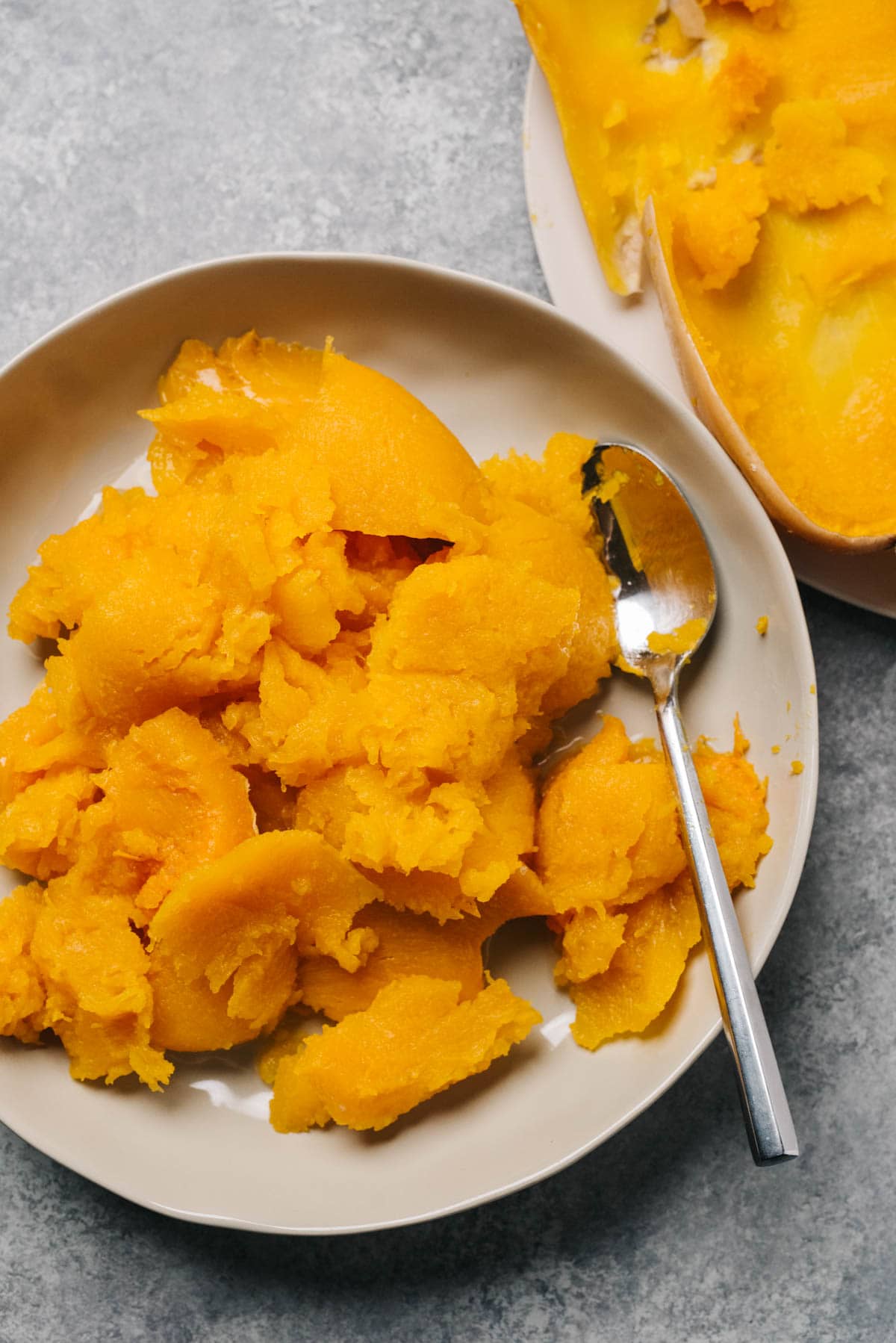 The flesh from slow cooker butternut squash scooped out of the skin and transfer to a low tan bowl.