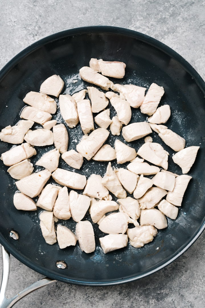 Stir fried pieces of chicken breast in a skillet.