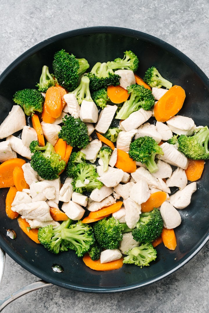 Chunks of chicken stir fried with broccoli and sliced carrots in a skillet.