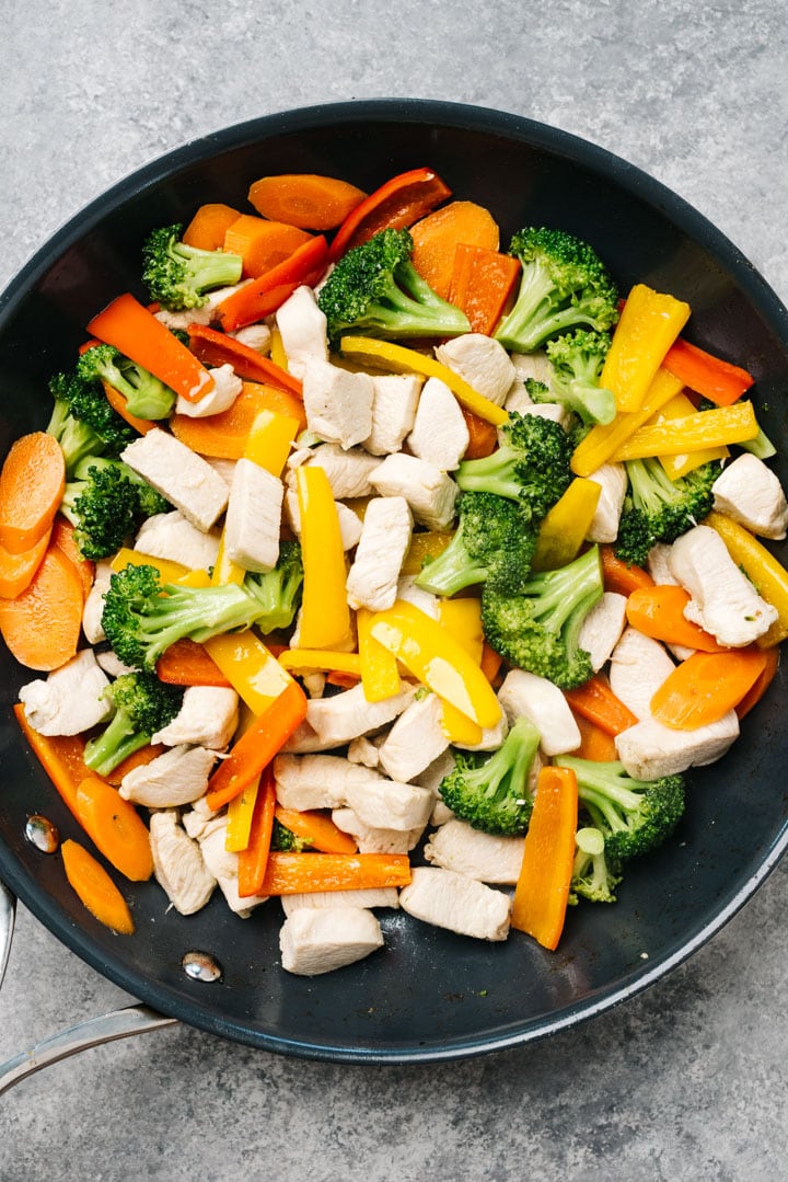 Stir fried chicken and vegetables (broccoli, carrots, and bell peppers) in a skillet.