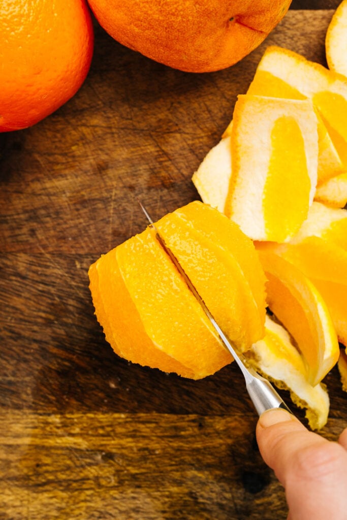 Slicing into a peeled orange to removed a segment of fruit.