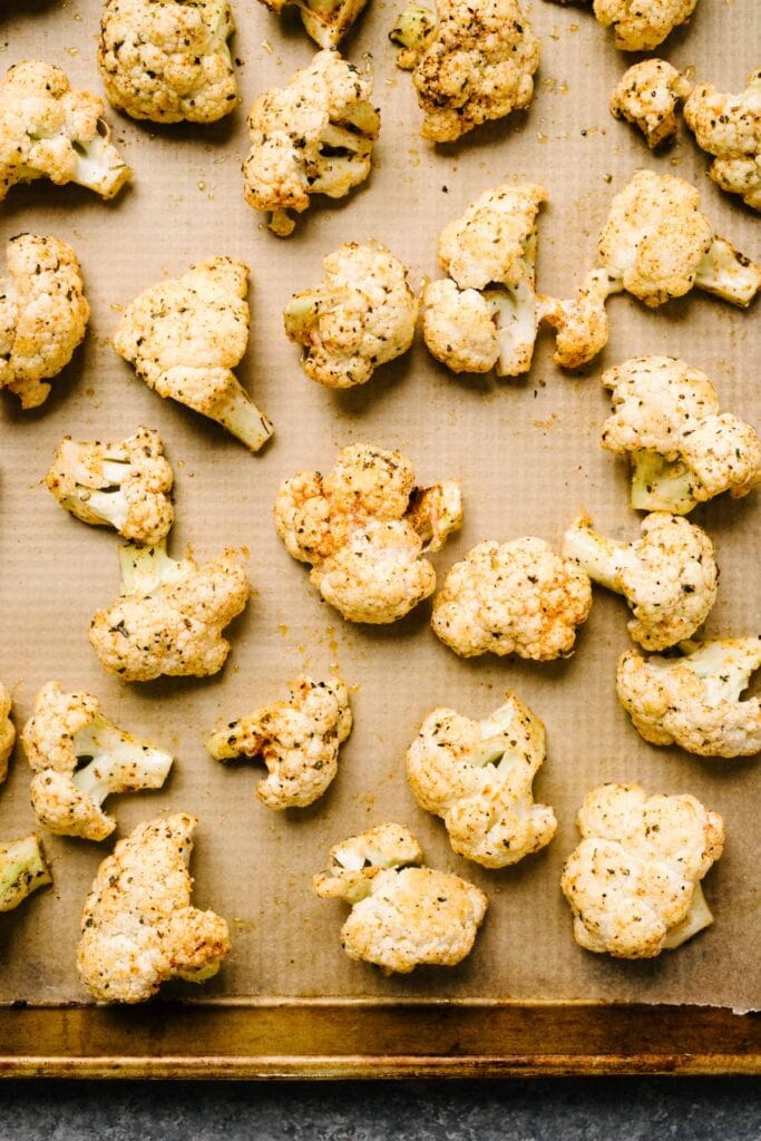 Oiled and seasoned raw cauliflower florets arranged in a single, even layer on a parchment lined baking sheet.