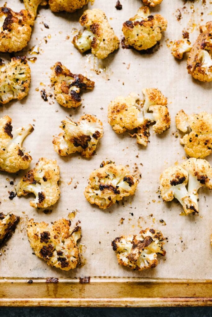 Roasted cauliflower florets on a parchment lined baking sheet fresh from the oven.