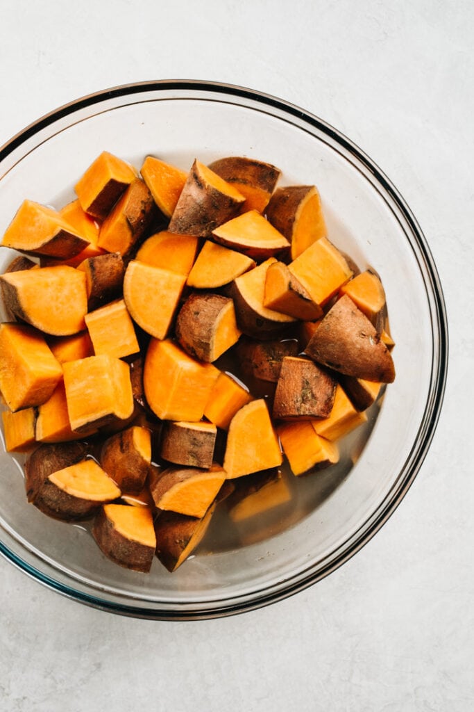 Par-cooked sweet potatoes in a glass bowl with water.