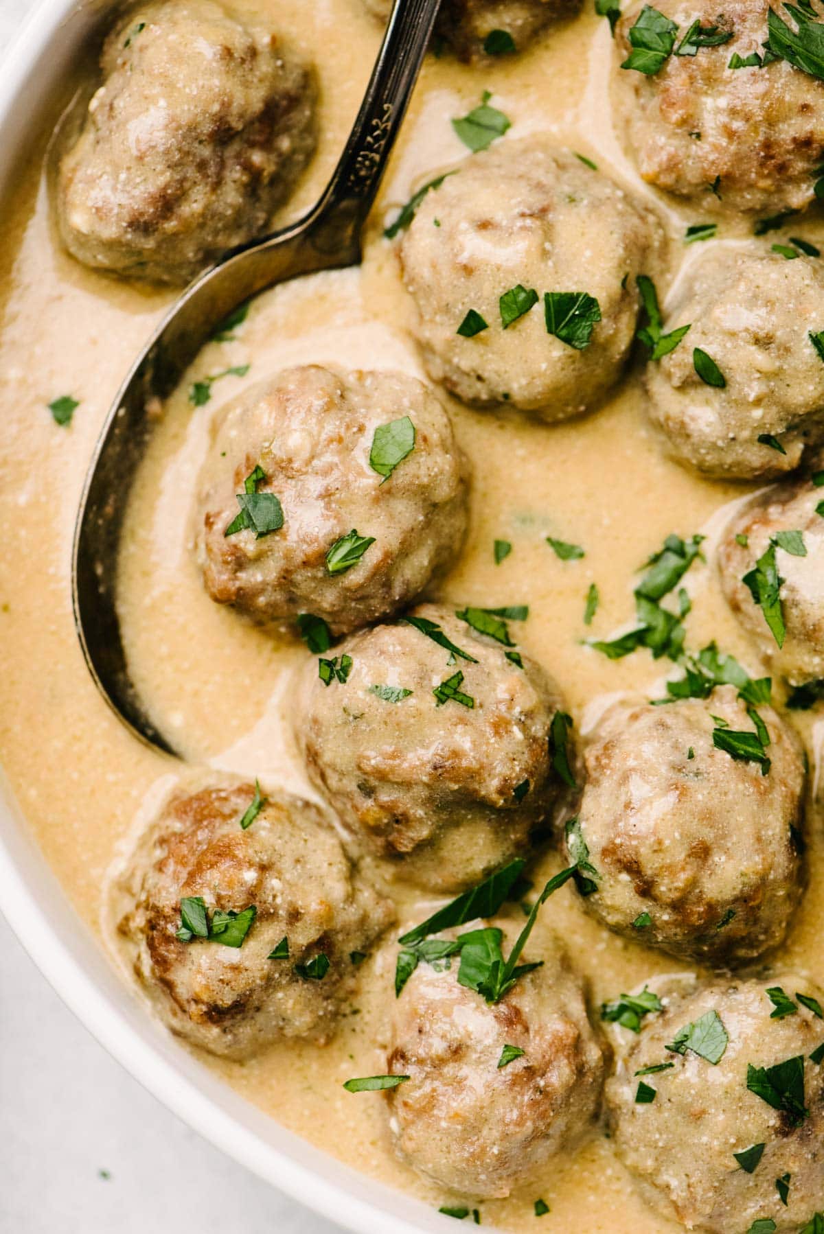 Crockpot Swedish meatballs in a low white serving bowl with a silver serving spoon.