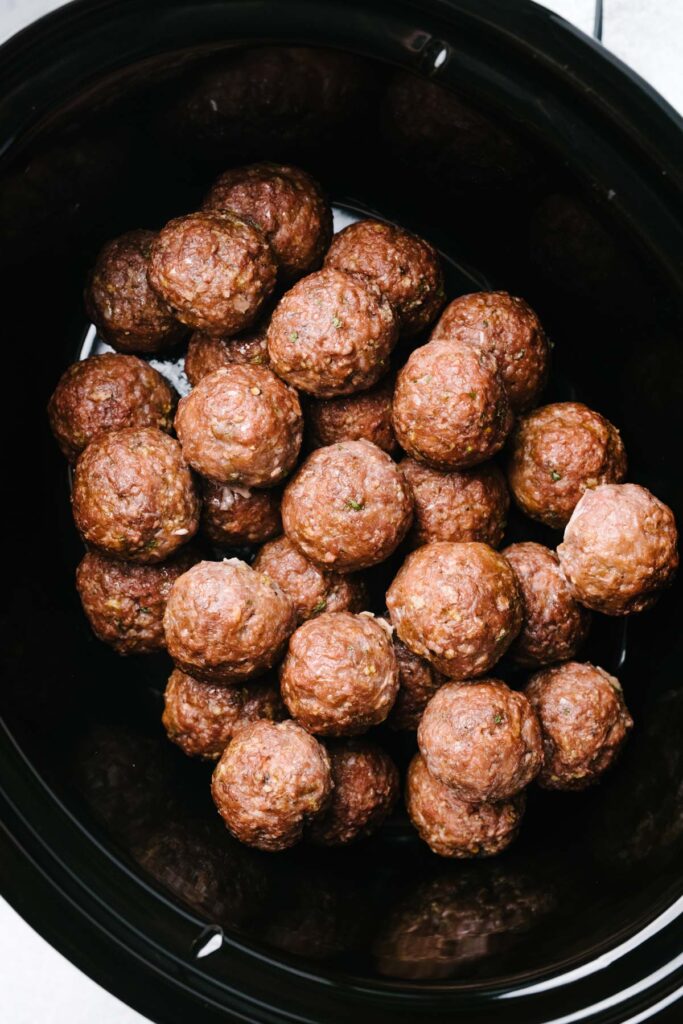 Browned Swedish meatballs arranged in a slow cooker.