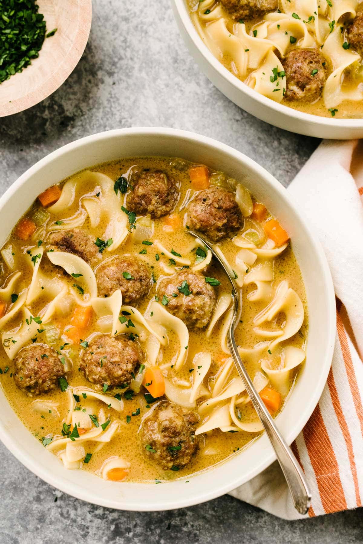 Two bowls of Swedish meatball soup garnished with fresh parsley with a striped linen napkin to the side.