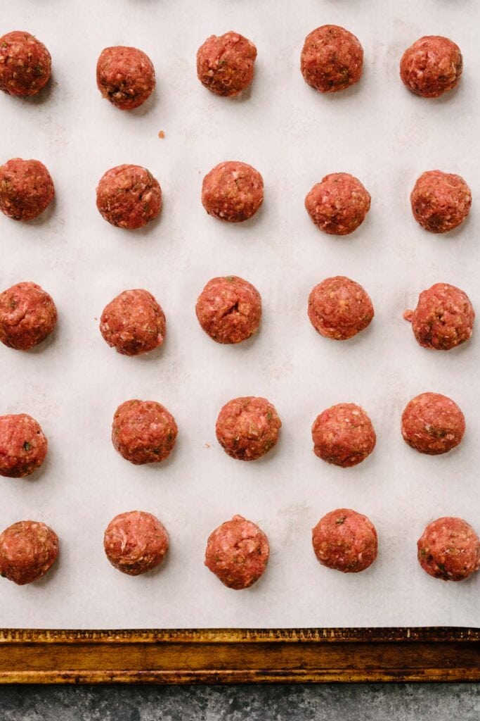 Mini Swedish meatballs arranged on a parchment lined baking sheet before browning in the oven.