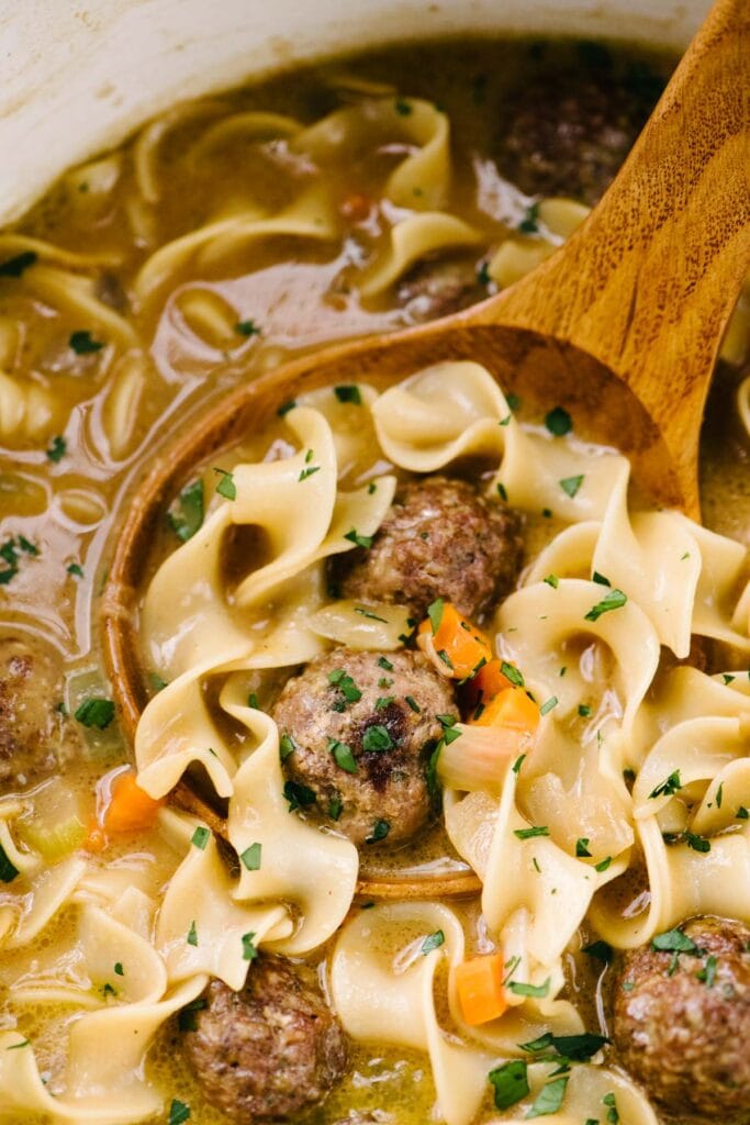 Side view, a wood ladle tucked into a pot of Swedish meatball soup, garnished with fresh parsley.