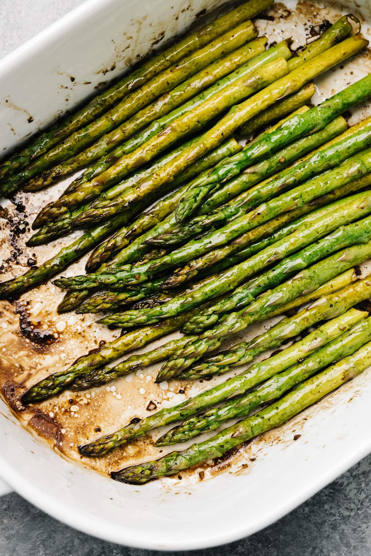 Baked asparagus spears with balsamic vinegar in a white casserole dish.