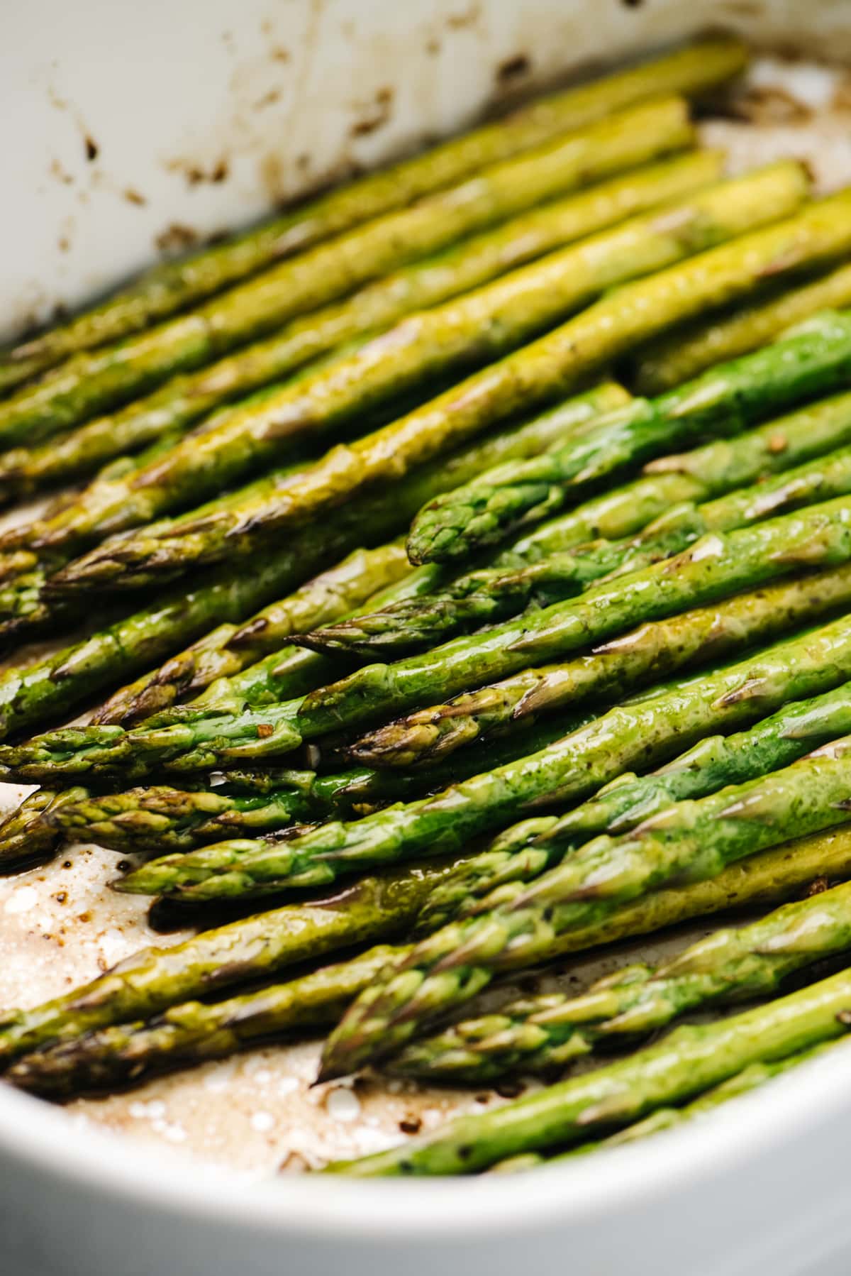 Side view, baked asparagus spears with tender stalks and crispy tips in a white casserole dish.