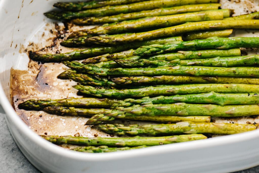 Side view, tender baked asparagus with balsamic vinegar in a casserole dish.