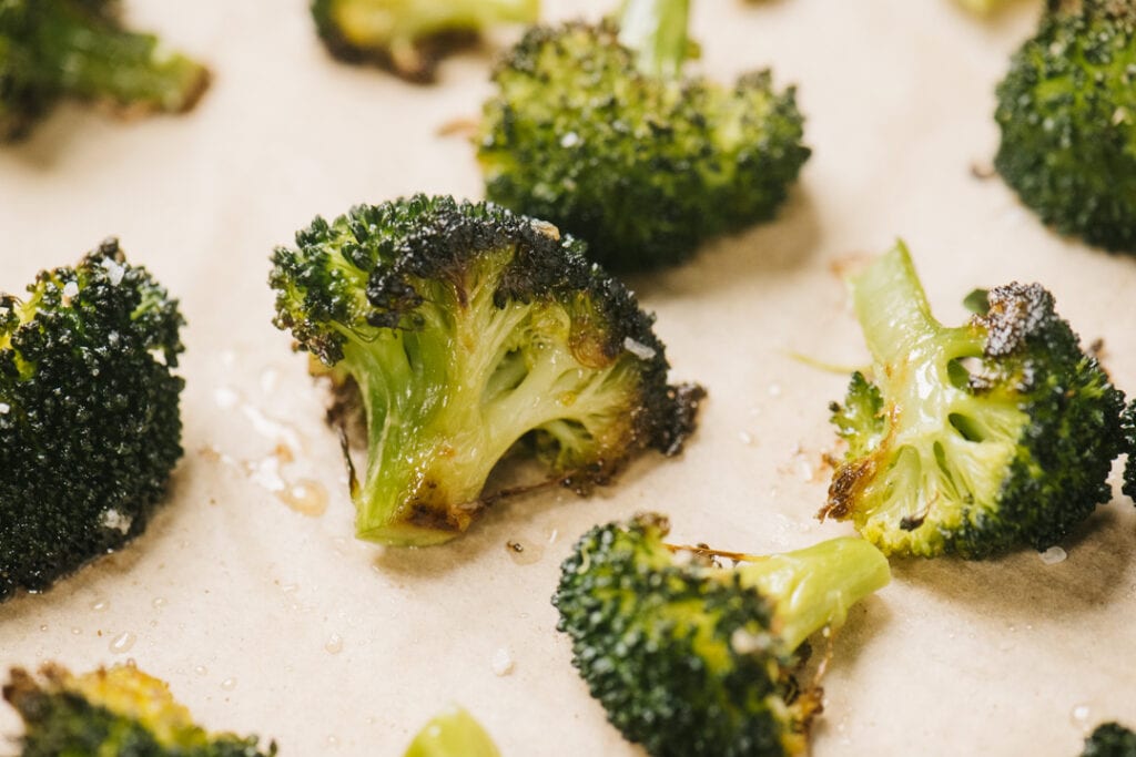 Side view, oven roasted broccoli florets on a parchment lined baking sheet.