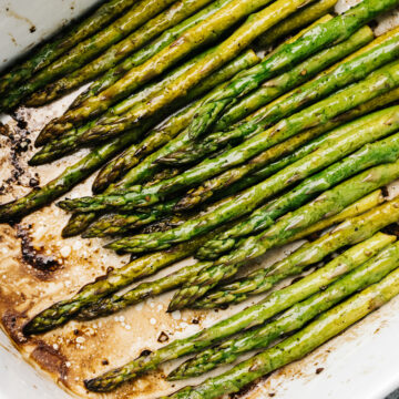 Baked asparagus with balsamic vinegar in a white casserole dish.