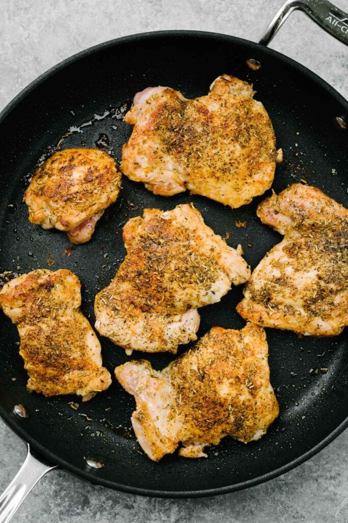 Seasoned boneless chicken thighs seared until golden brown in a skillet.