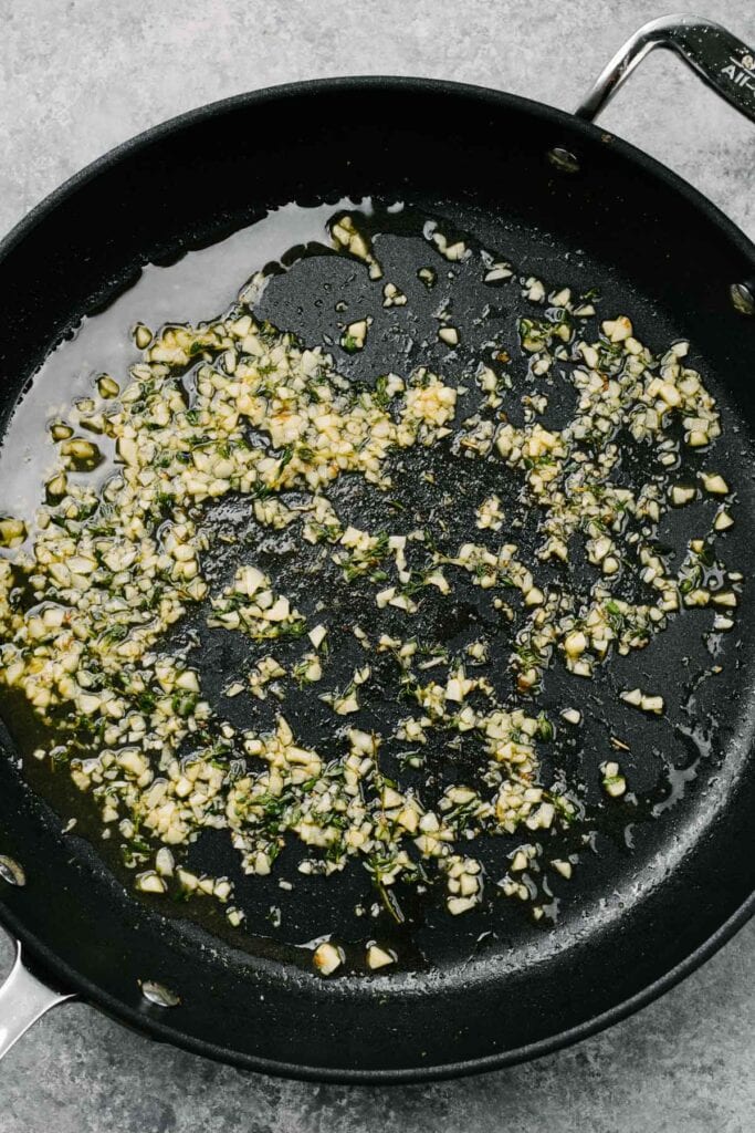 Sautéed garlic and thyme deglazed with white wine in a skillet.