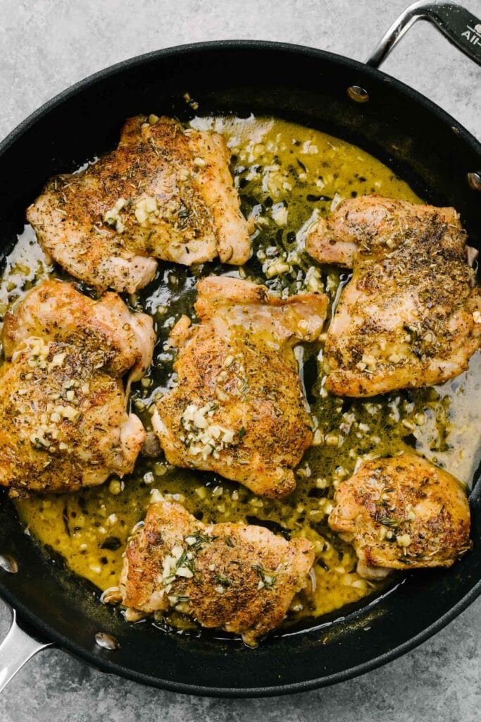 Sautéed garlic butter chicken thighs with fresh thyme in a skillet.