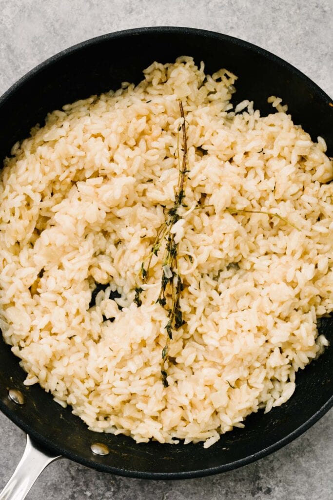 Cooked risotto rice with a thyme sprig in a skillet.