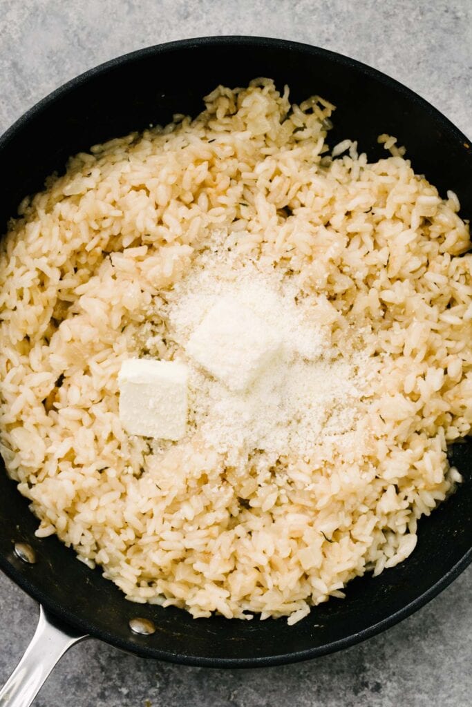 Butter and parmesan cheese added to a skillet of cooked risotto.