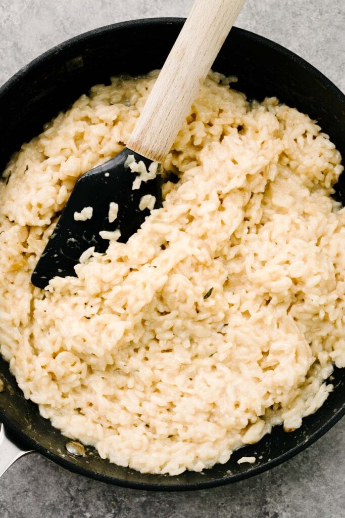 A rubber spatula tucked into a skillet of easy creamy risotto rice.