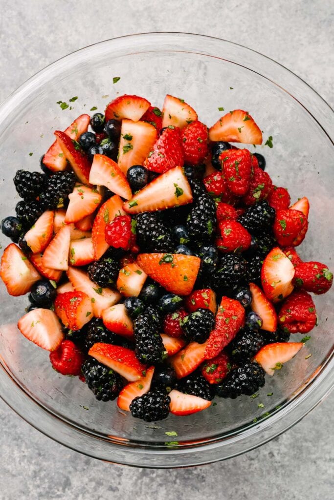Mixed berry salad with honey lemon dressing in a large glass mixing bowl on a concrete background.